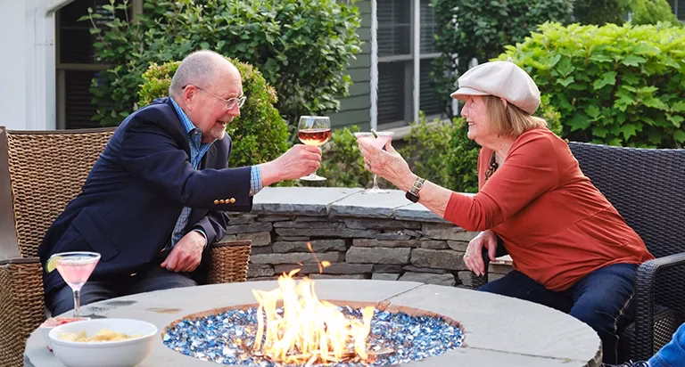Man and woman toasting with drinks next to outdoor fire pit