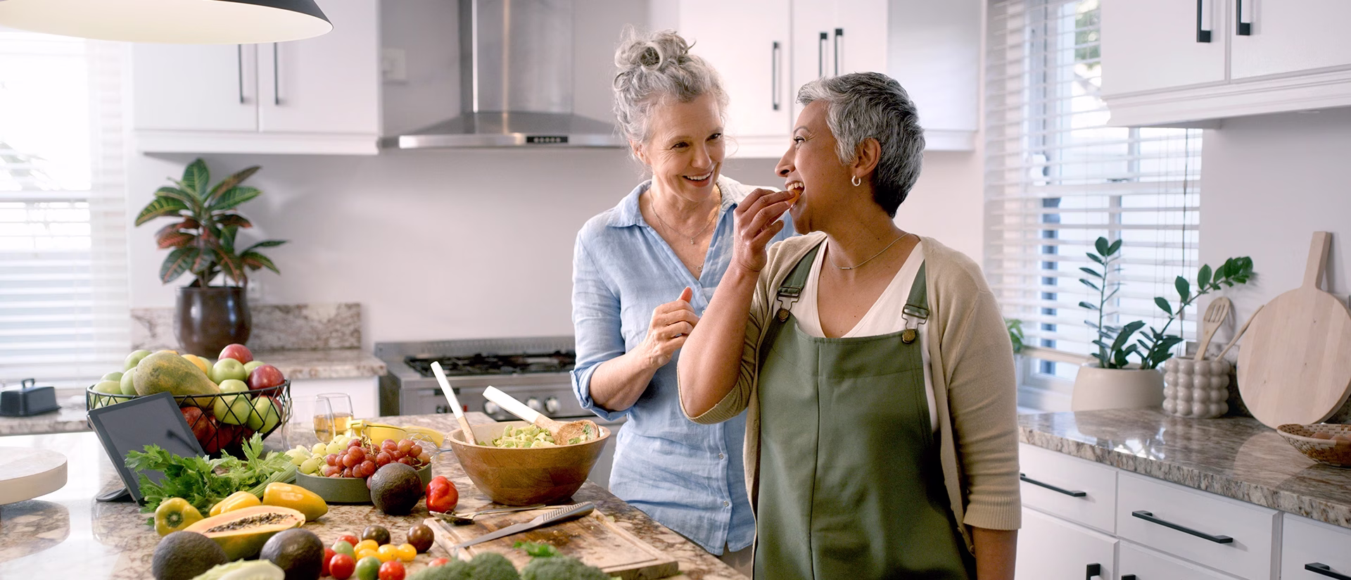 Two women preparing fruit salad in kitchen